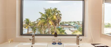 A bathroom with a large window, two sinks, and a view of palm trees and a river.