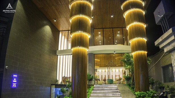 A modern hotel lobby with a grand staircase, illuminated columns, and a reception desk. - An Phu Hotel (Phu Quoc)