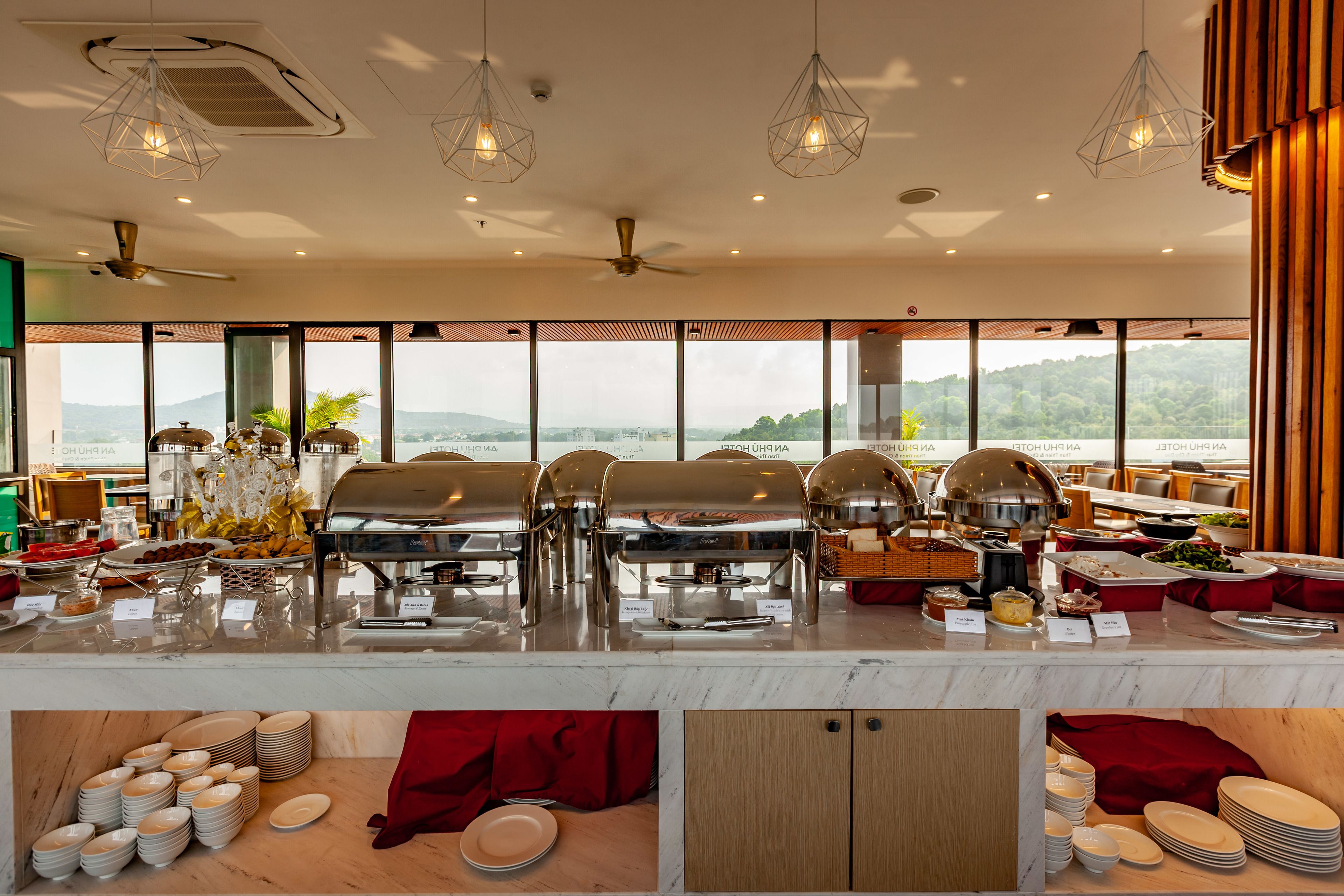 A buffet setup with multiple food stations, a ceiling fan, and large windows offering a scenic view.