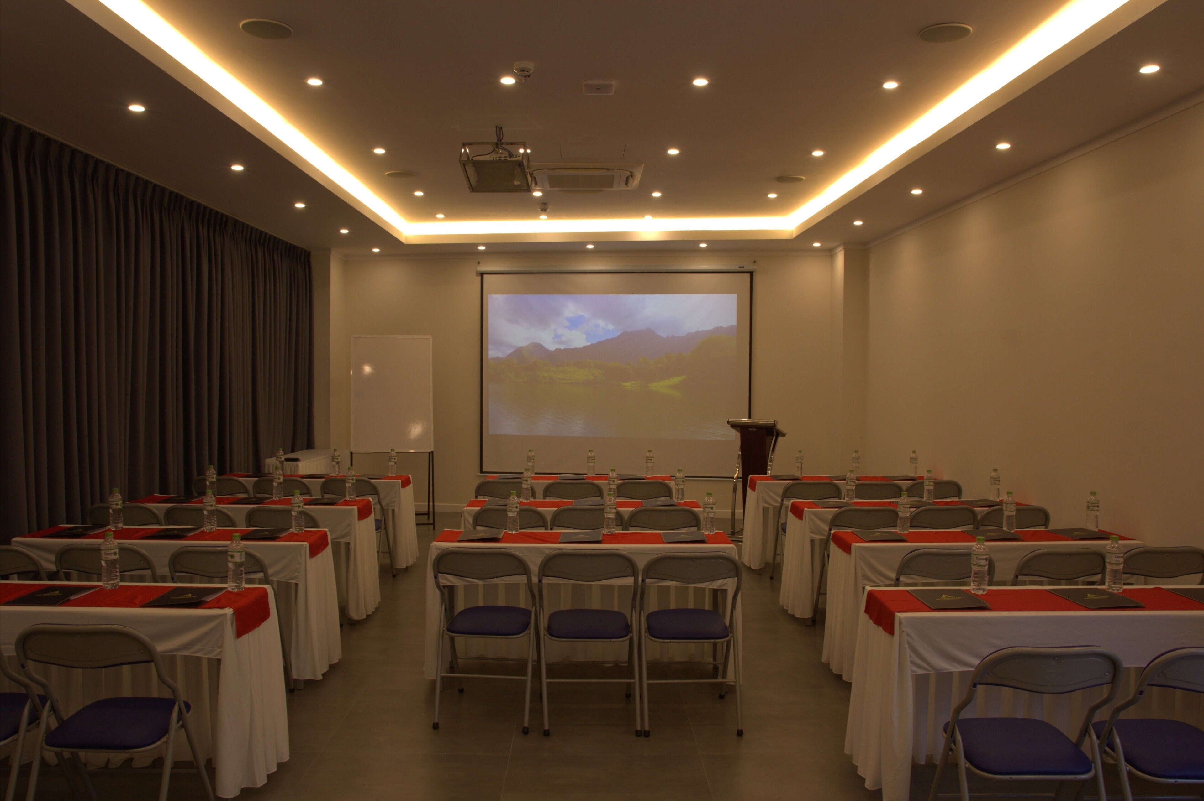 A conference room with rows of tables and chairs, a projector screen, and a podium.