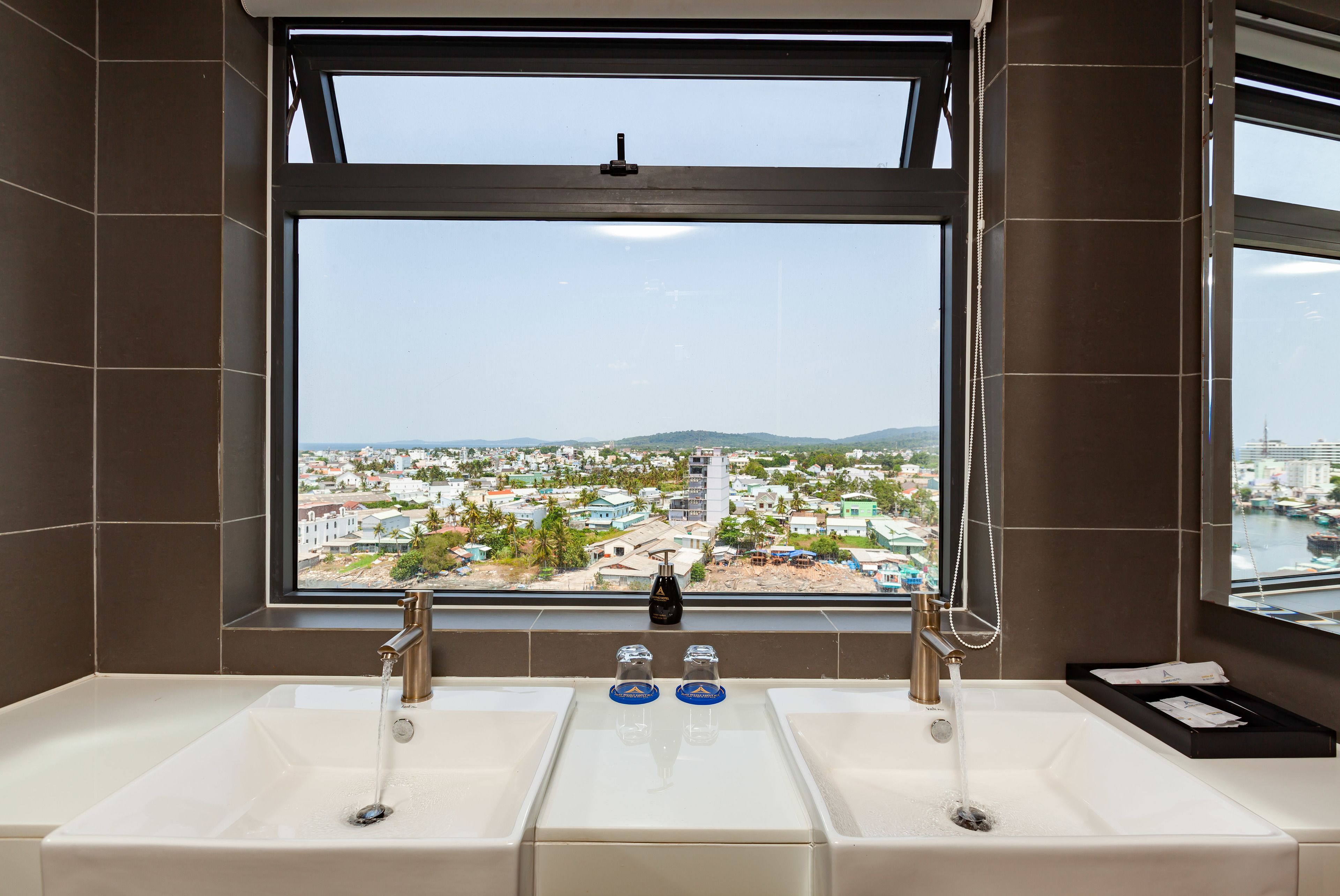 A bathroom with a large window, two sinks, and a view of a cityscape.