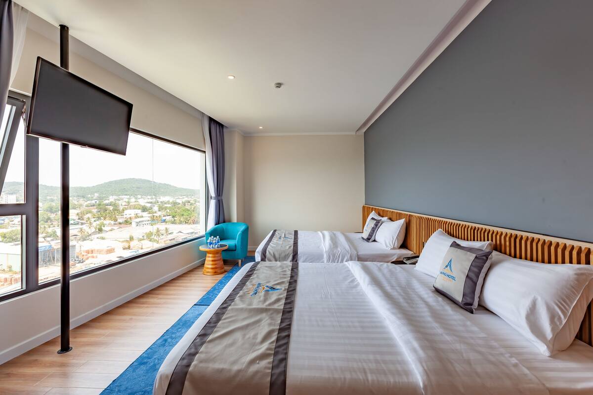 Habitación de hotel con una cama grande, televisión y vista a un paisaje urbano.