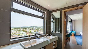 A modern bathroom with a large window, dual sinks, and a view of a cityscape. - An Phu Hotel (Phu Quoc)