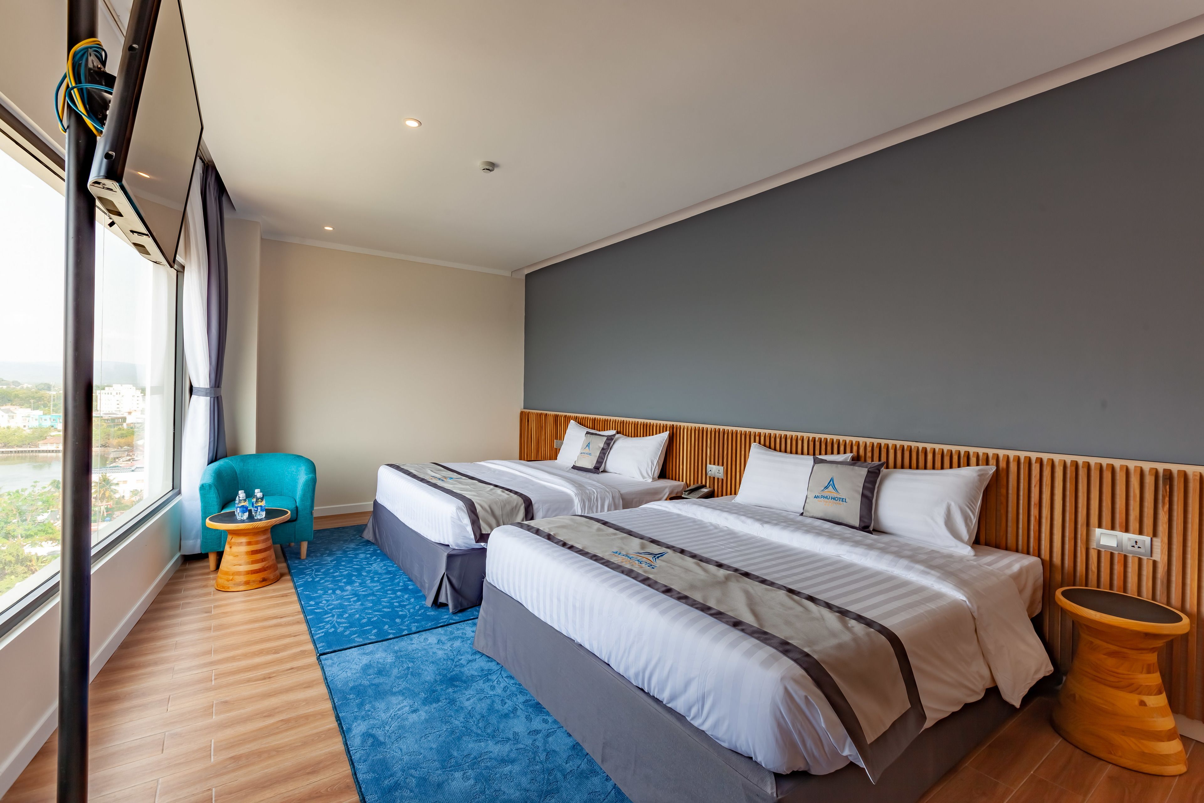 Une chambre d’hôtel avec deux lits, une moquette bleue, une tête de lit en bois et une vue sur la ville.