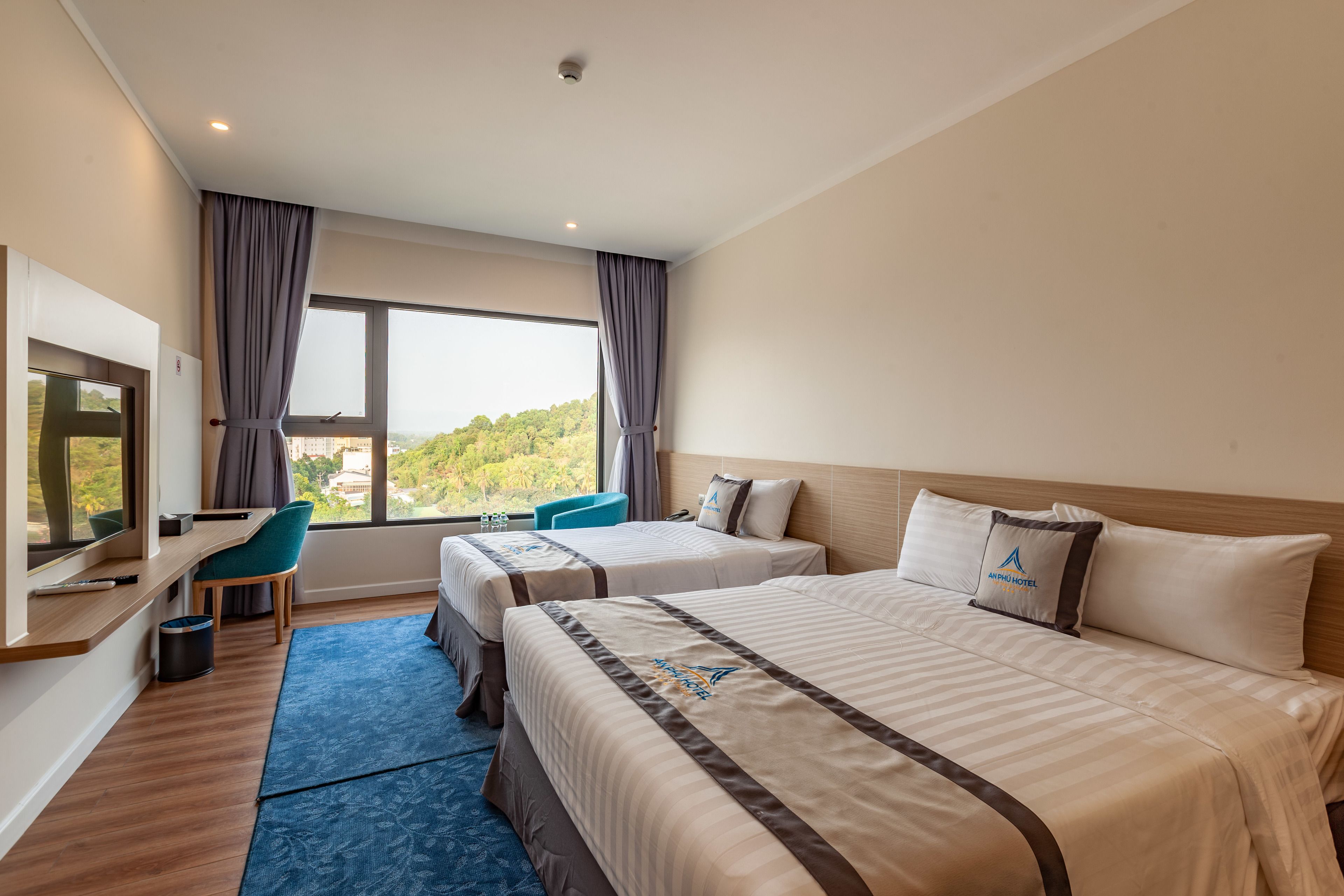 A hotel room with two beds, a desk, a chair, and a large window offering a view of the outdoors.