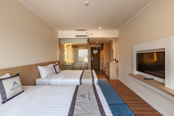 Ein Hotelzimmer mit zwei Betten, einem Fernseher und einem durch eine Glastür einsehbaren Badezimmer.