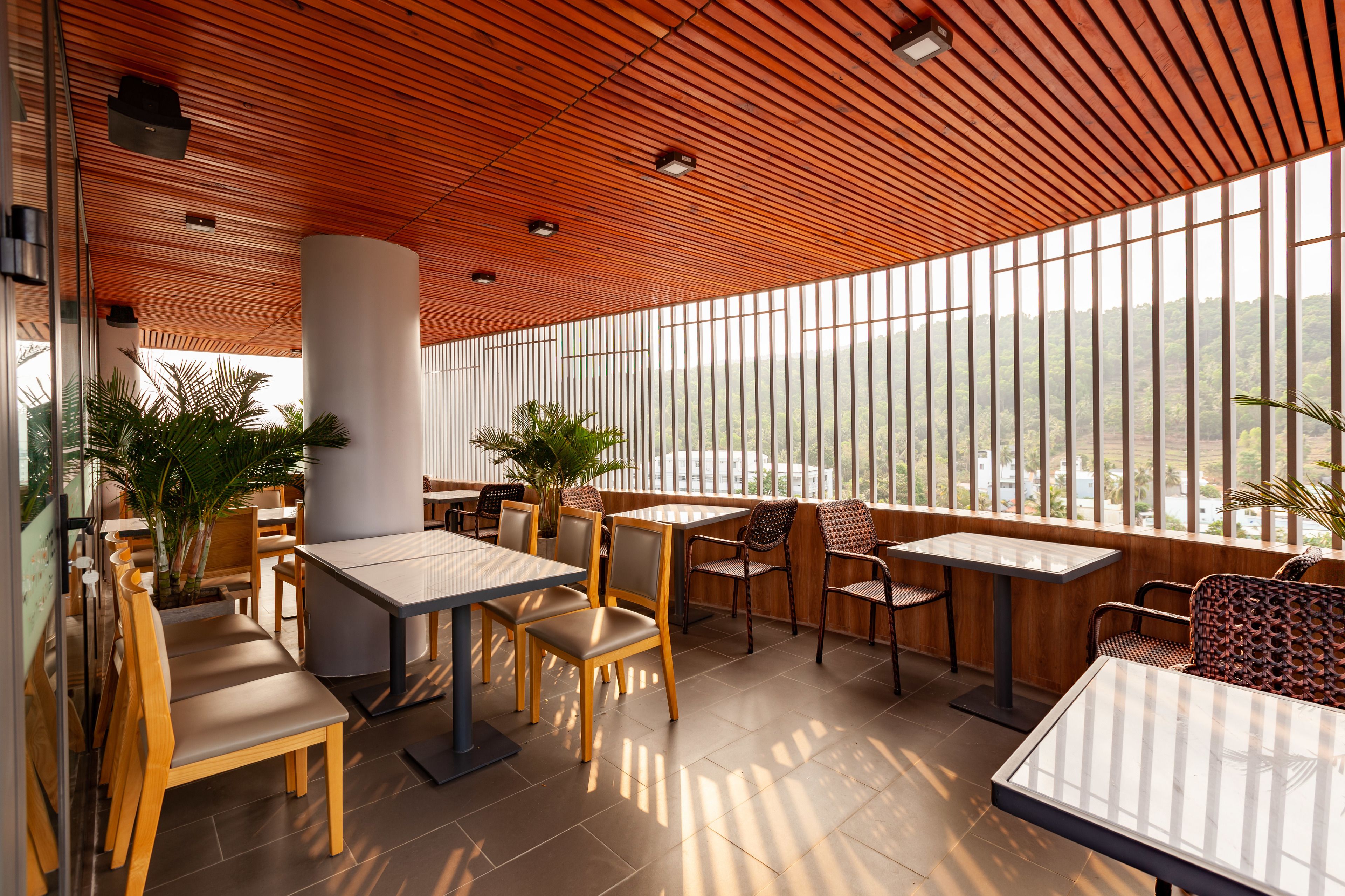 Ein Restaurant mit Holzbalkendecken, großen Fenstern und Zimmerpflanzen.