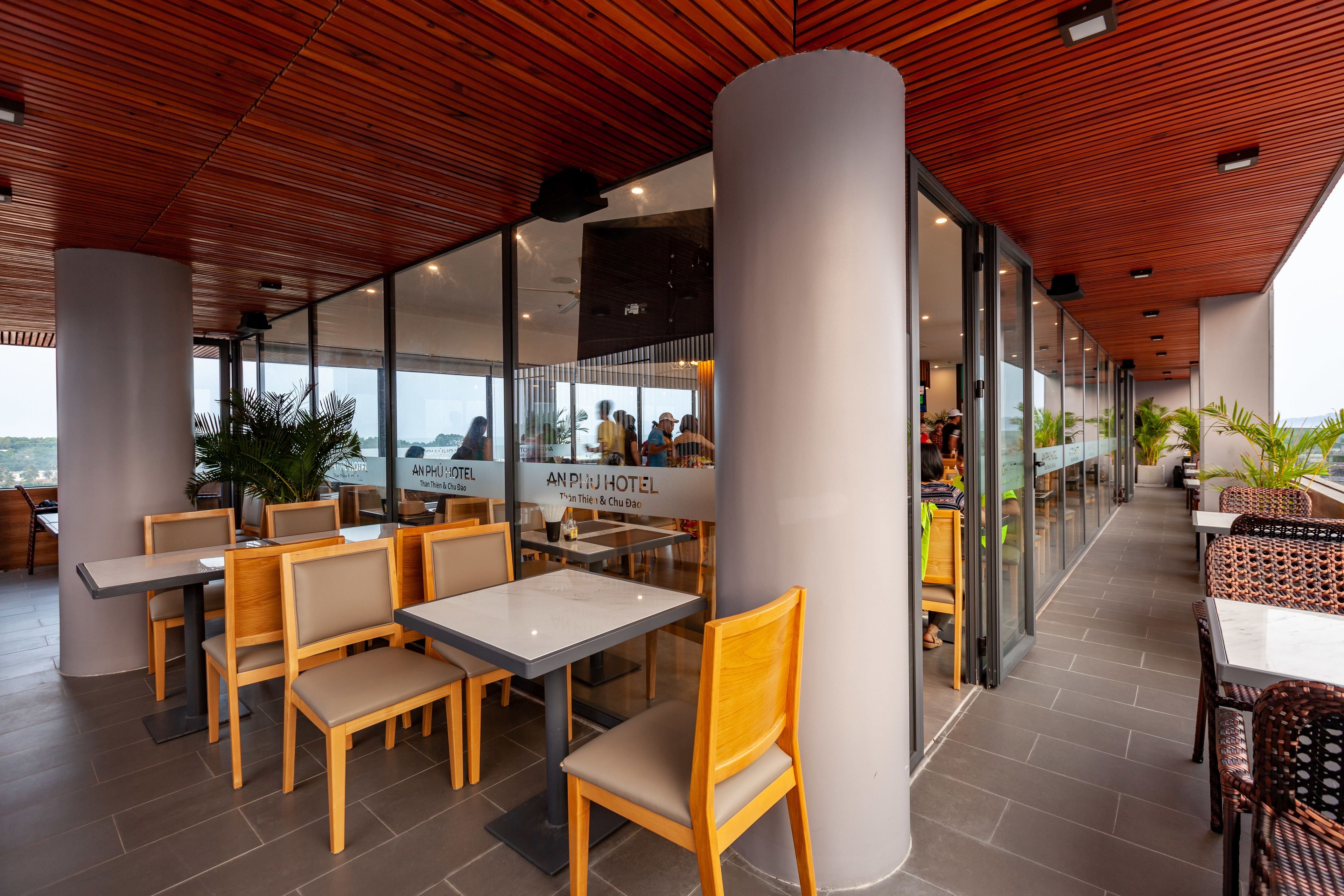 A modern hotel restaurant with wooden ceiling, glass walls, and outdoor seating.