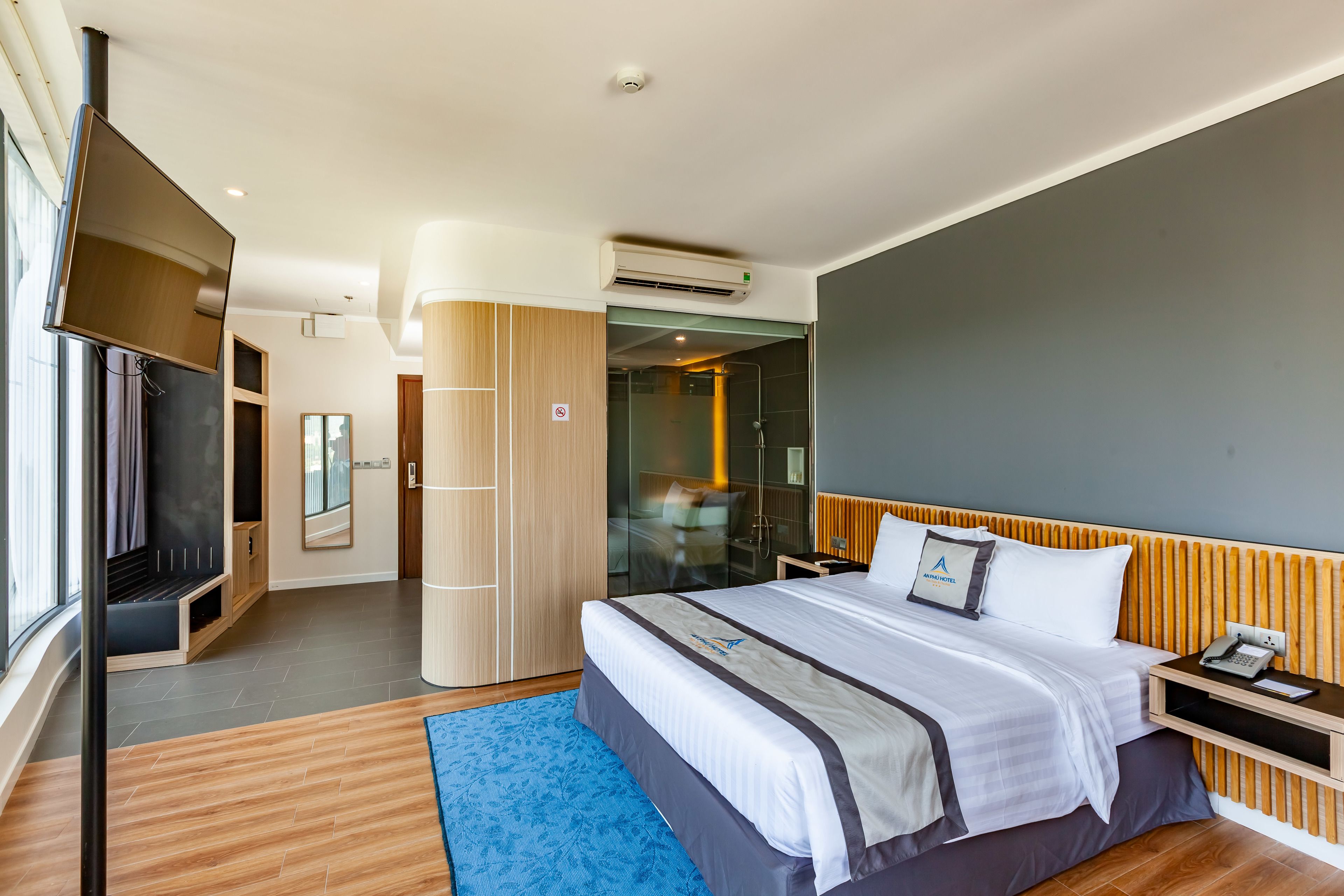 A modern hotel room with a large bed, a TV, a desk, and a bathroom visible through a glass door.