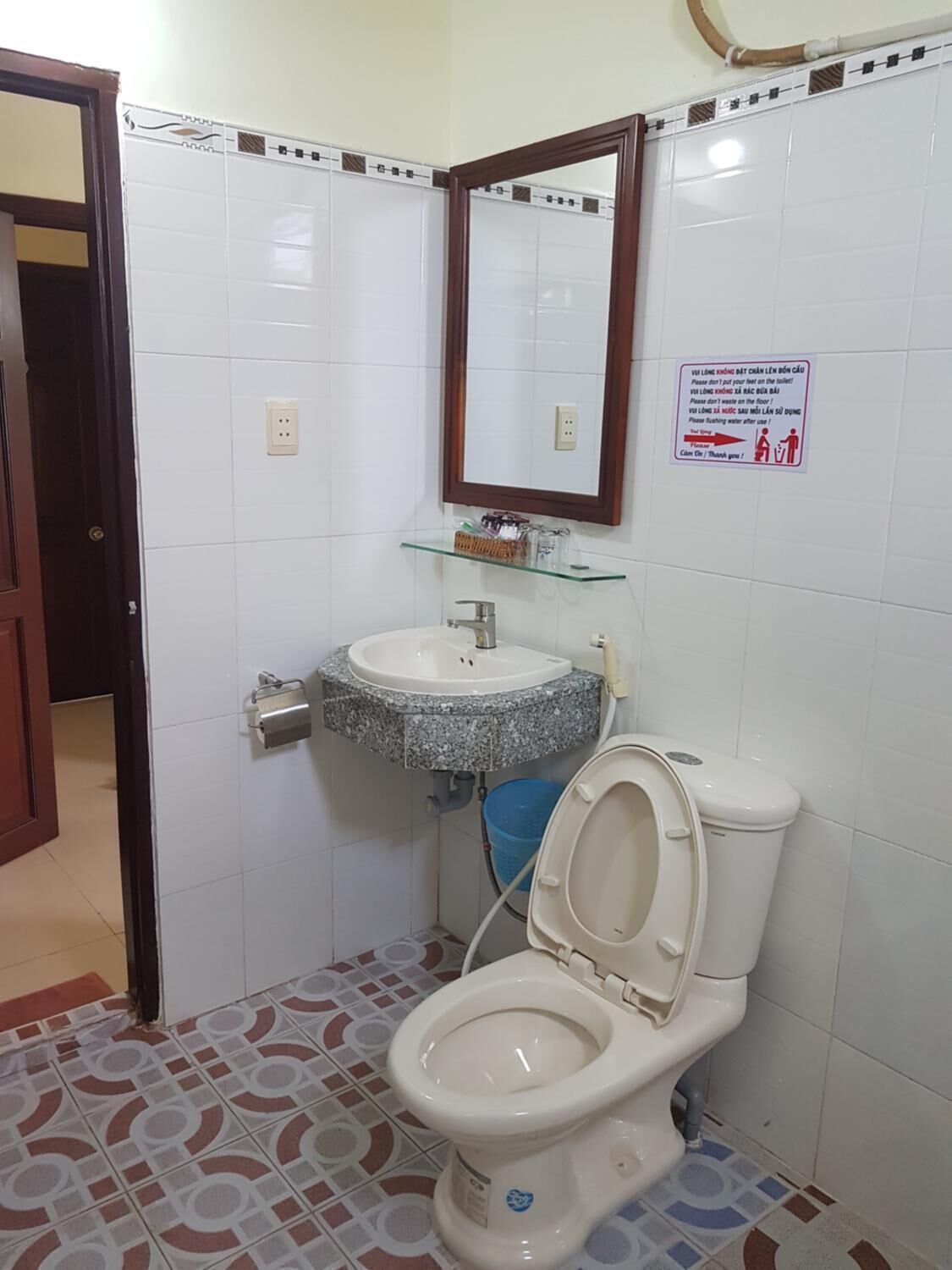 A bathroom with a white toilet, a granite sink, and a mirror above it. There is a sign on the wall with instructions.
