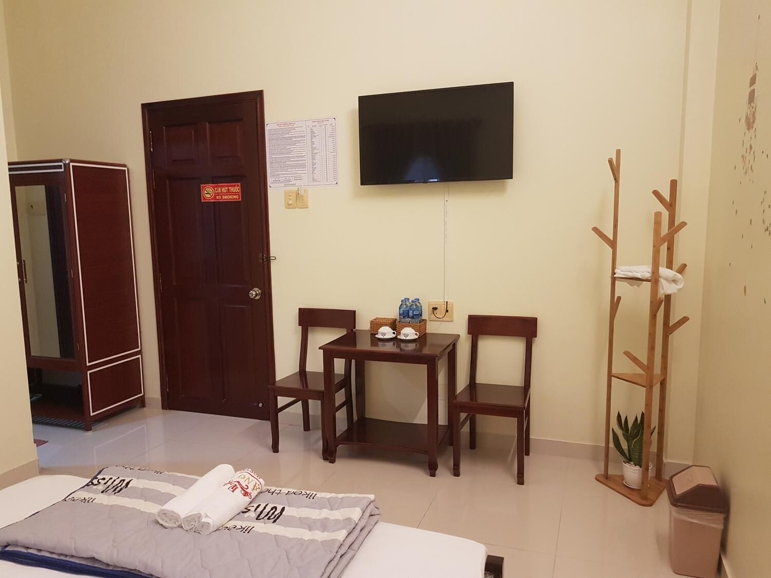 Habitación de hotel con cama, escritorio con sillas, televisor, perchero y un aviso en la puerta.