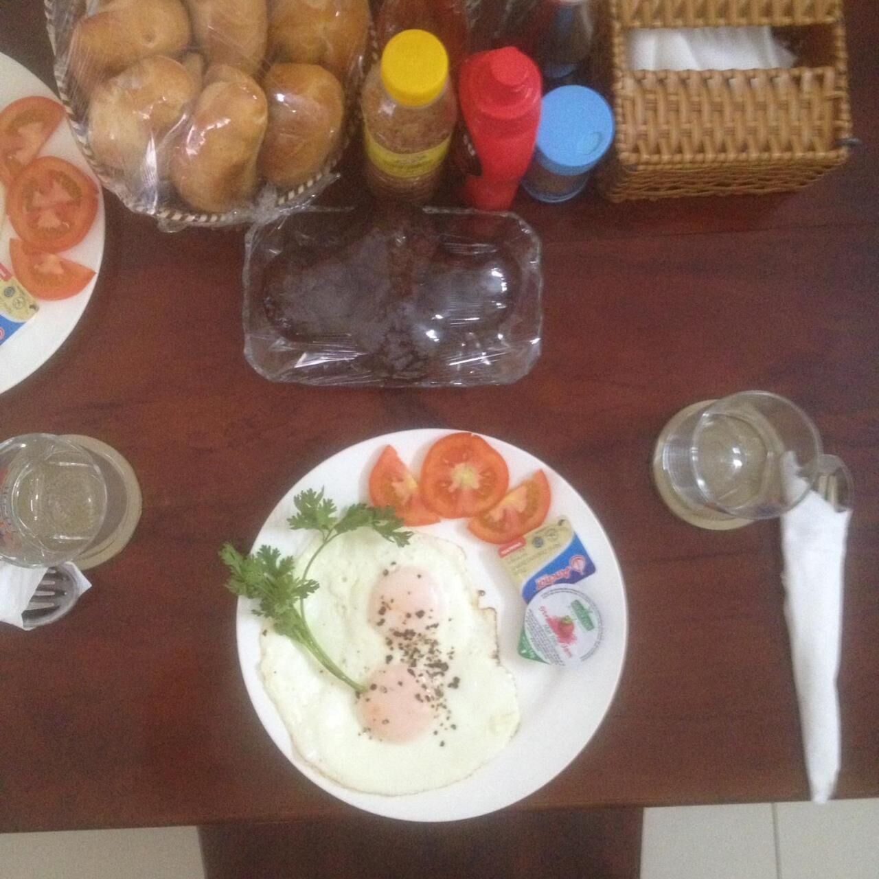Ein Frühstückstisch mit Eiern, Tomaten, Petersilie, einem Brötchenkorb, Gewürzen und einem Glas Wasser.