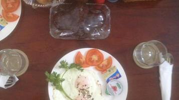 Ein Frühstückstisch mit Eiern, Tomaten, Petersilie, einem Brötchenkorb, Gewürzen und einem Glas Wasser.