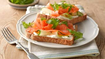 A plate with two pieces of toast topped with smoked salmon, cream cheese, cucumber, and arugula.