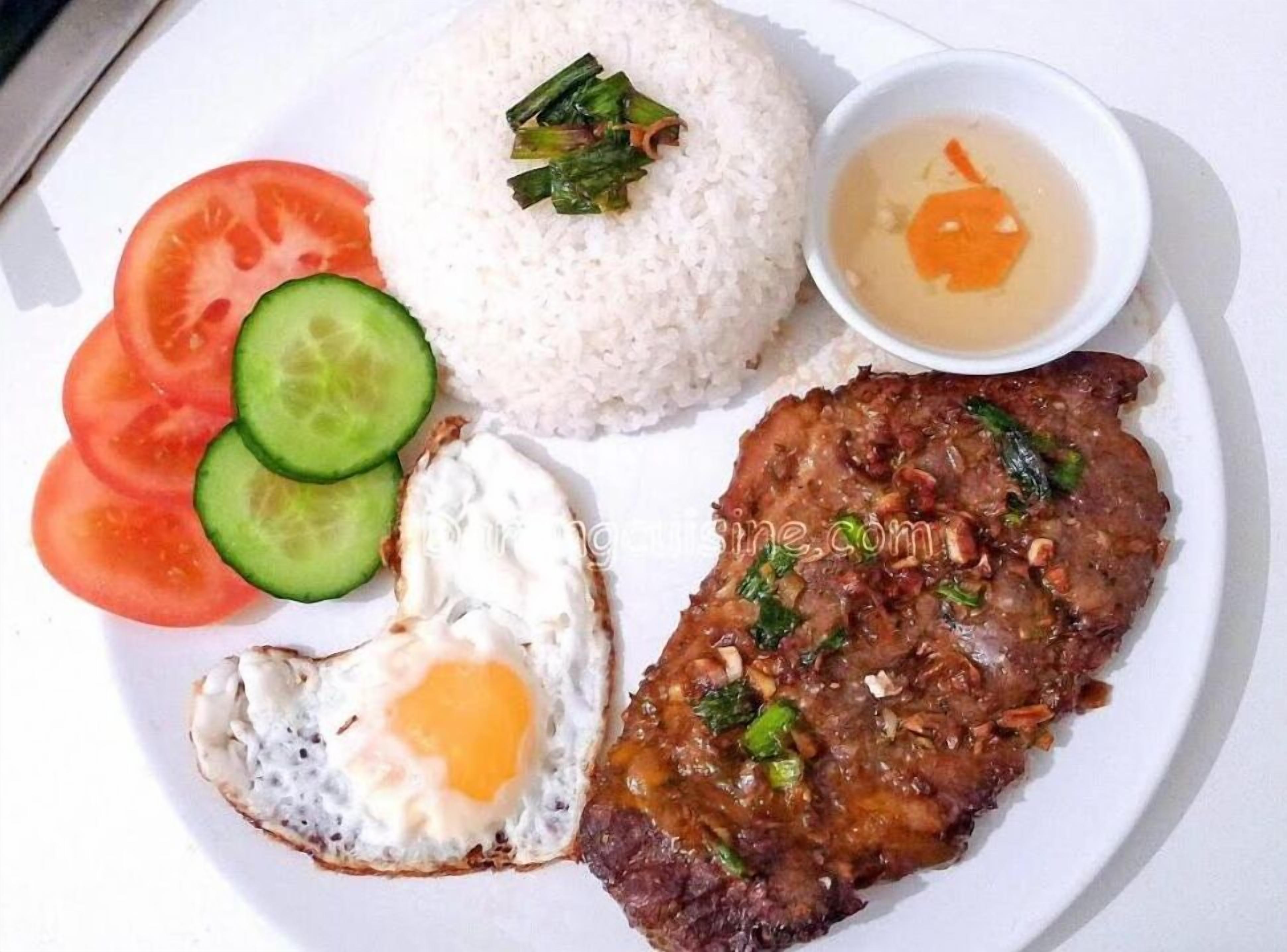 A plate with rice, a fried egg, a meat dish, slices of tomato, cucumber, and a small bowl of soup.