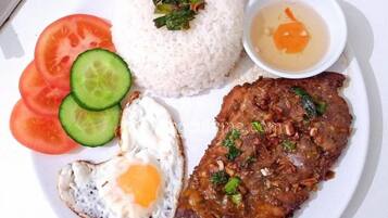 A plate with rice, a fried egg, a meat dish, slices of tomato, cucumber, and a small bowl of soup.
