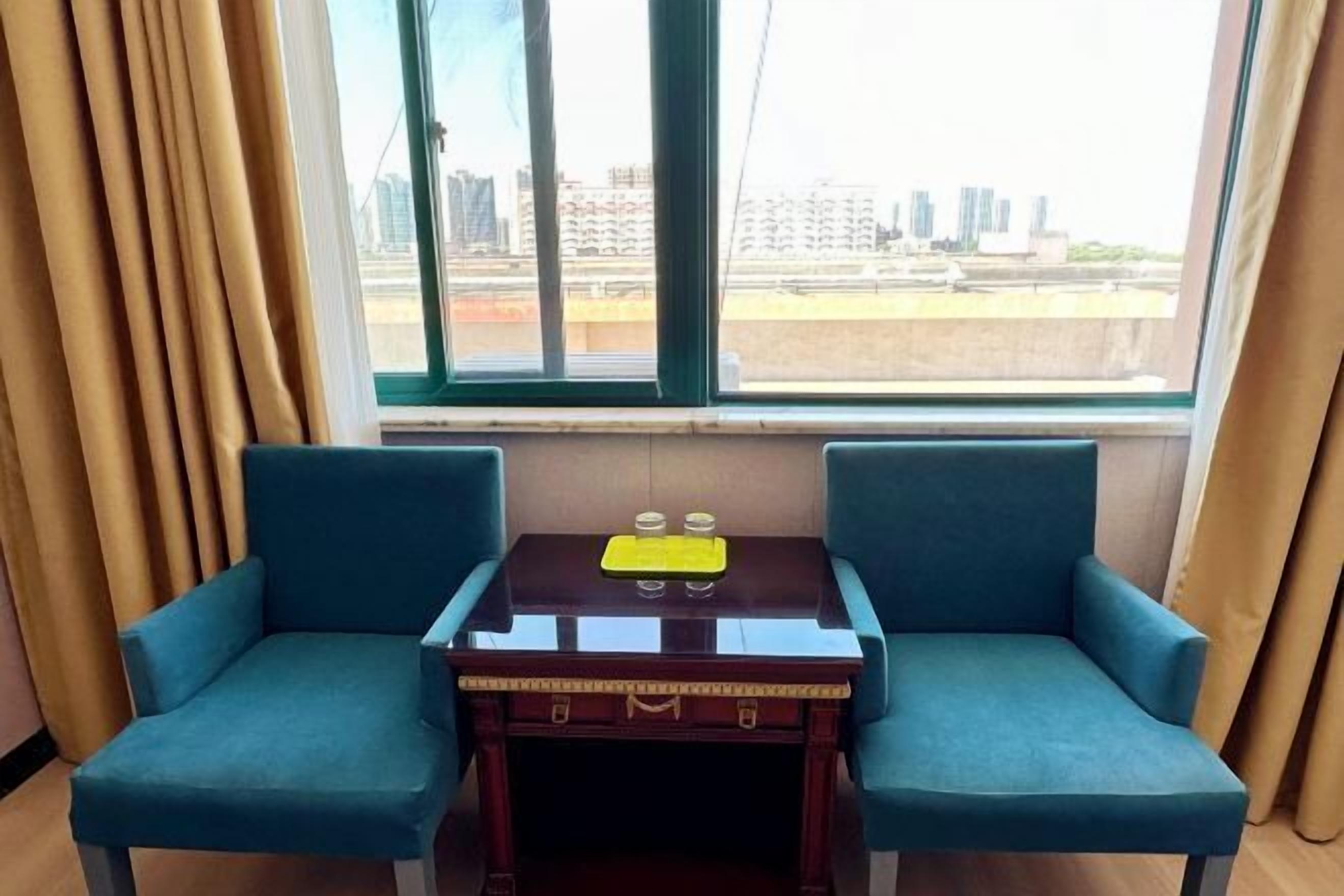Una habitación con dos sillones azules, una pequeña mesa de madera con una bandeja y un ventanal con vistas a la ciudad.