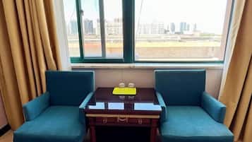 Una habitación con dos sillones azules, una pequeña mesa de madera con una bandeja y un ventanal con vistas a la ciudad.