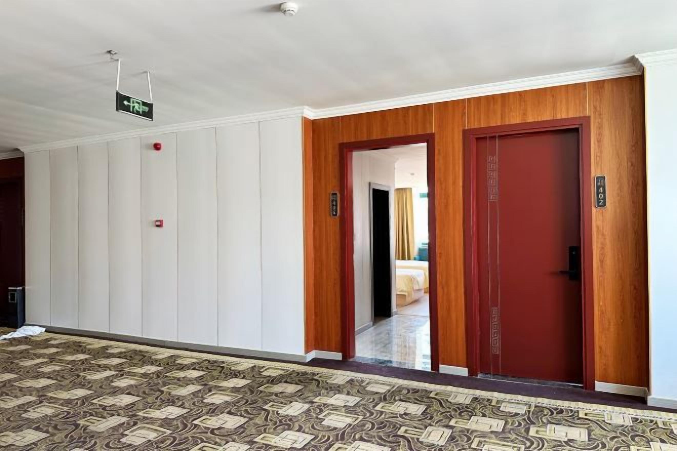 Ein Hotelgang mit einem gemusterten Teppich, einer roten Tür und einem Schild, das den Weg zur Rezeption weist.