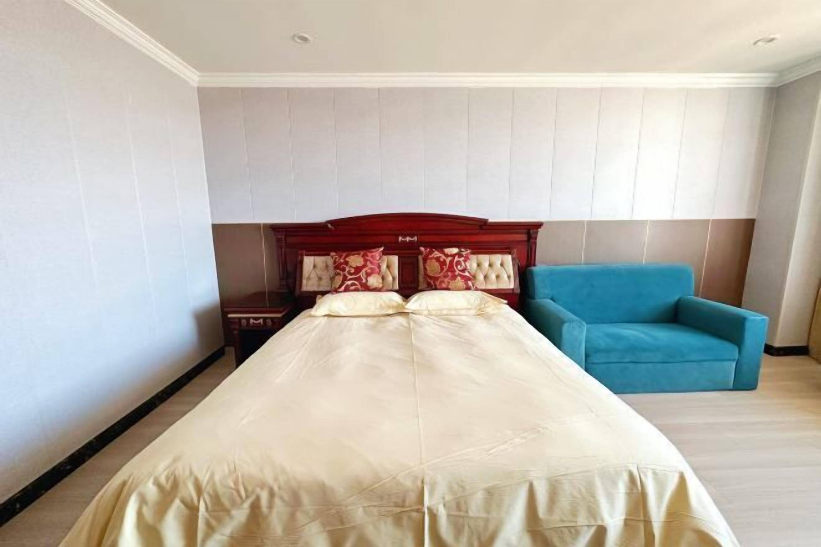 Quarto de hotel com uma cama grande, cabeceira de madeira e uma poltrona azul.