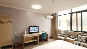 Habitación de hotel con una cama, un escritorio con computadora, una silla, una mesita y una ventana con cortinas.