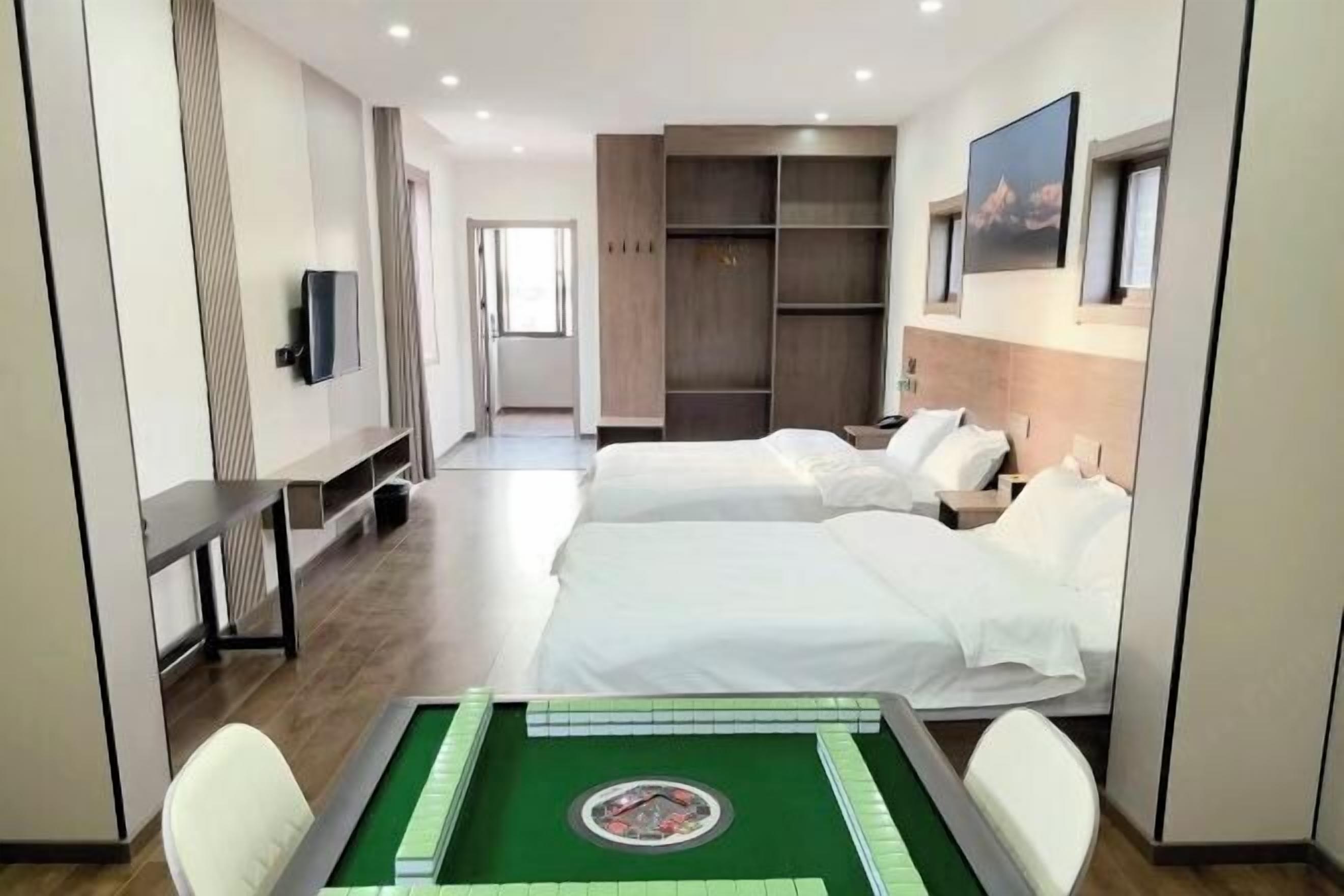 Ein Hotelzimmer mit zwei Betten, einem Schreibtisch, einem Fernseher, einem grünen Tisch mit Dekoration und einem Kleiderschrank.