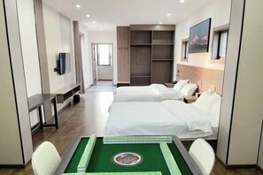 Ein Hotelzimmer mit zwei Betten, einem Schreibtisch, einem Fernseher, einem grünen Tisch mit Dekoration und einem Kleiderschrank.