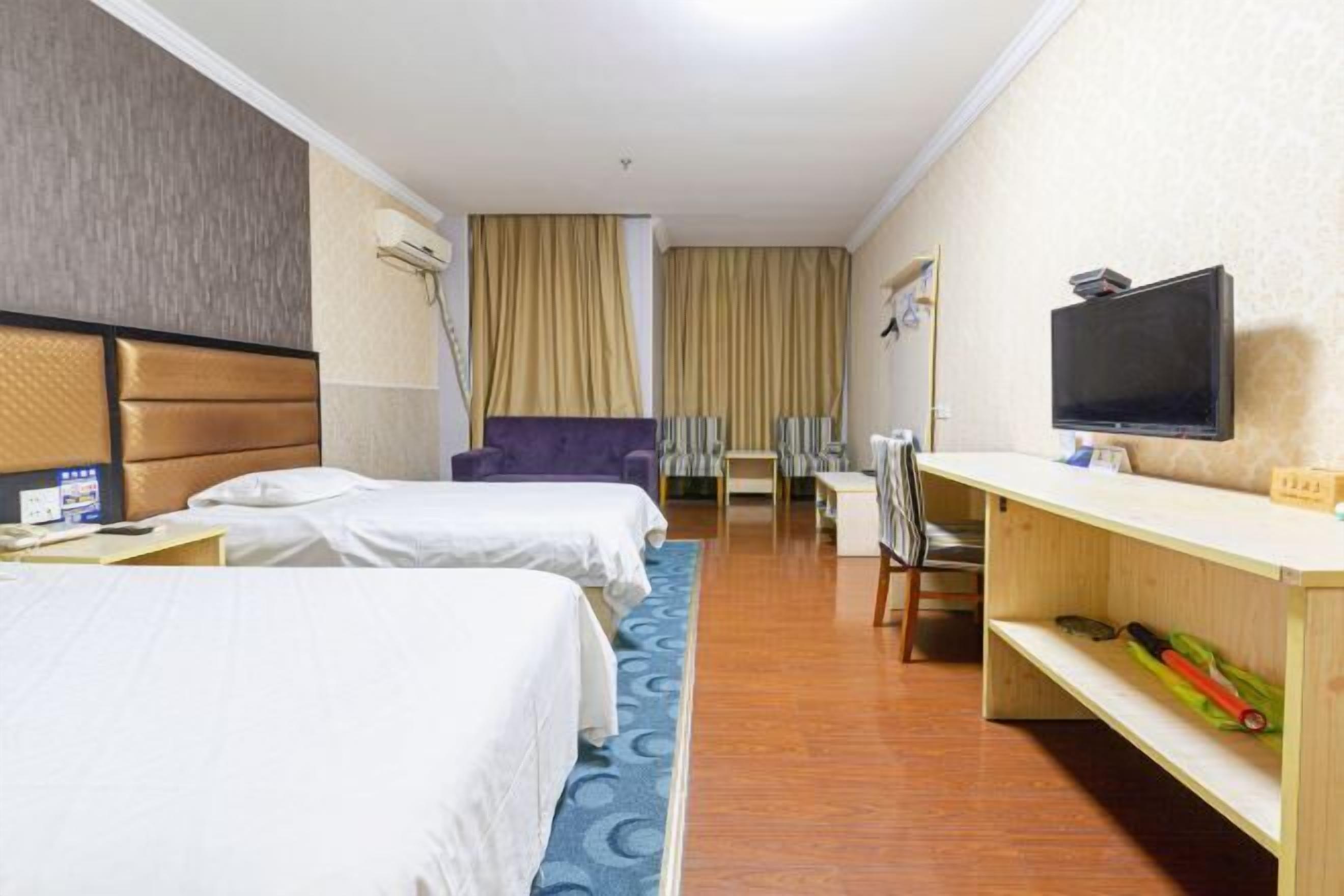 Ein Hotelzimmer mit zwei Betten, einem Schreibtisch, einem Sessel, einem Fernseher und einem Regal mit Gegenständen.