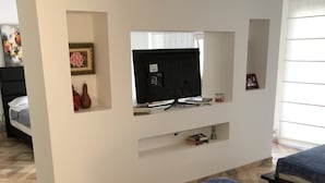 A hotel room with a bed, a TV mounted on the wall, and a small shelf with books and decorative items. - Villa Thiago Finca Tradicional (Armenia)