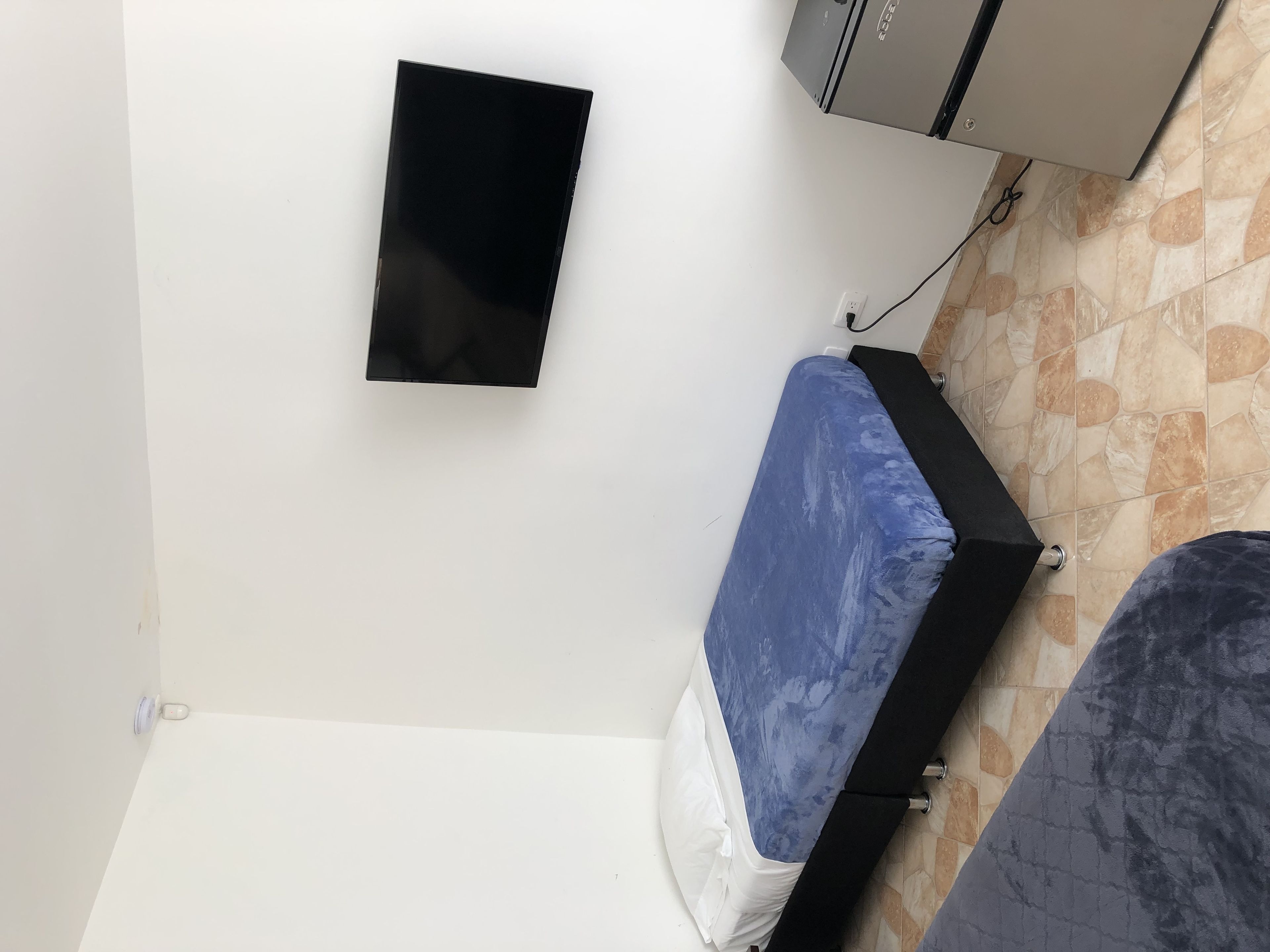 A room with a bed, a wall-mounted TV, and a tiled floor.