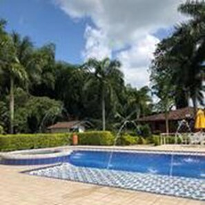 A swimming pool with a tiled deck, surrounded by palm trees and a clear sky.