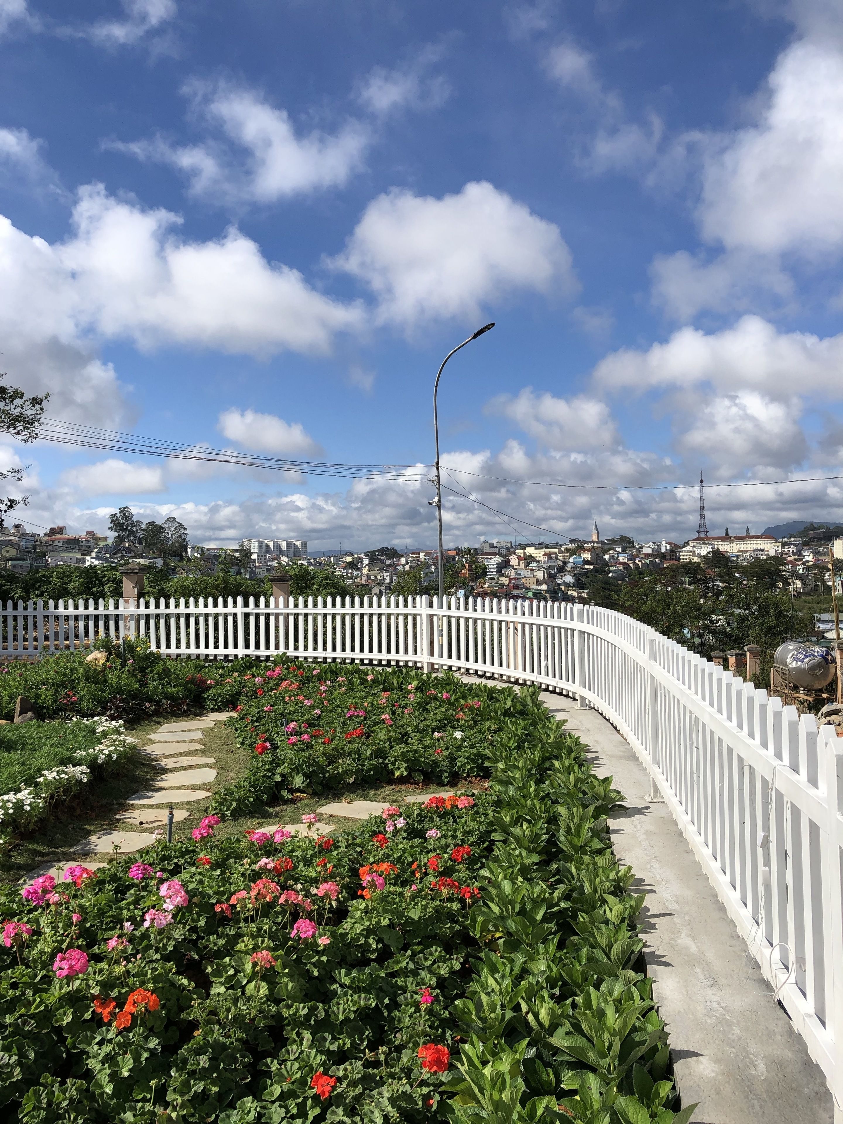 A garden with a white fence, a pathway, and a variety of flowers.