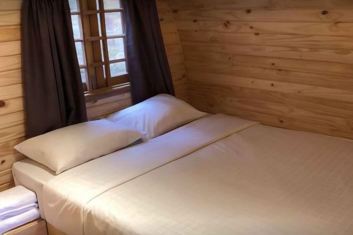 A wooden cabin room with a bed, curtains, and a window.