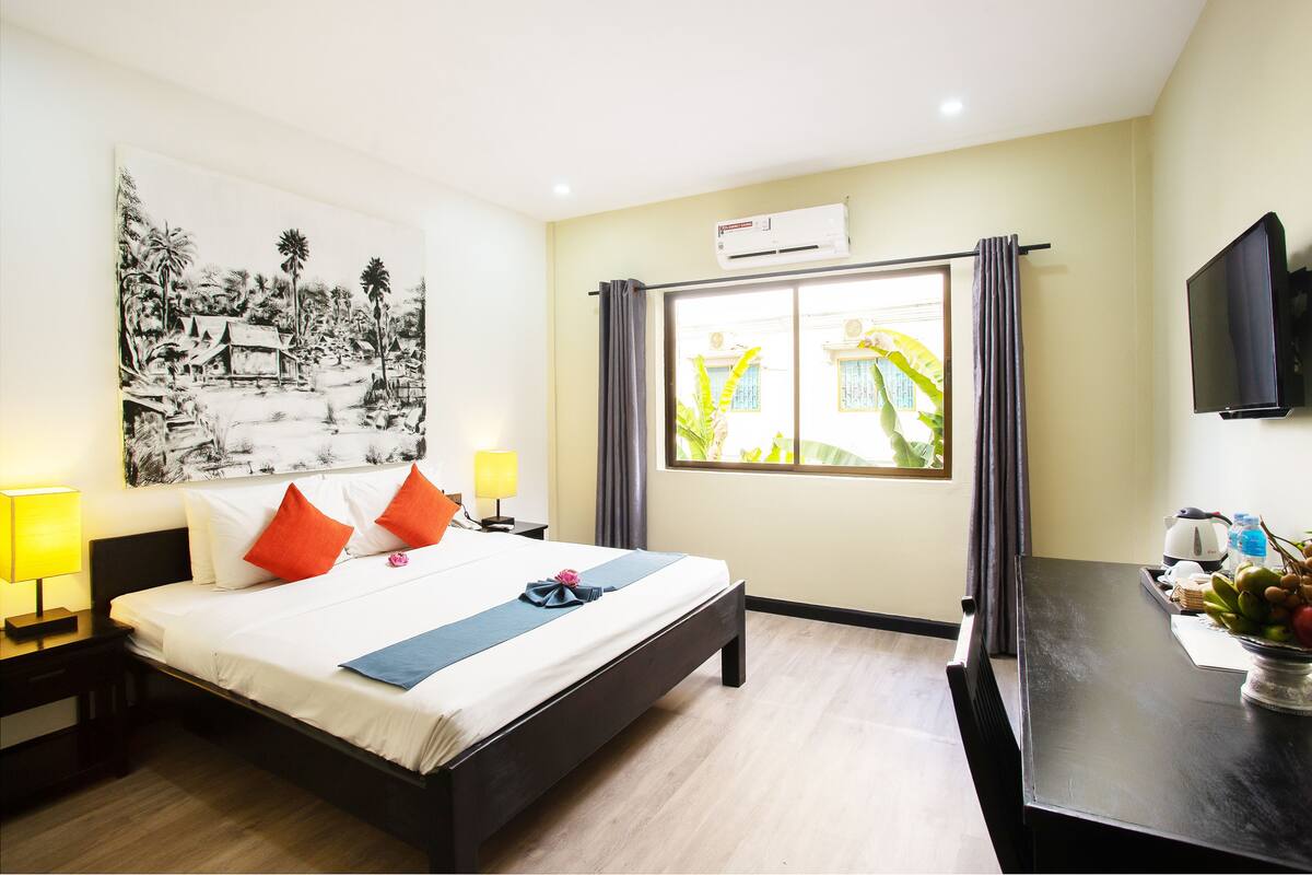 Een hotelkamer met een bed, nachtkastjes, een televisie, een raam met gordijnen en een schilderij aan de muur.