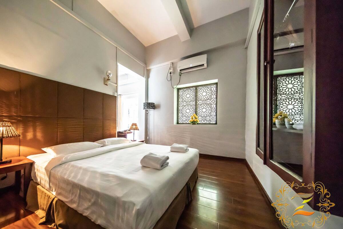 Camera d'albergo con un ampio letto, comodini, una finestra con un pannello decorativo e un condizionatore d'aria.