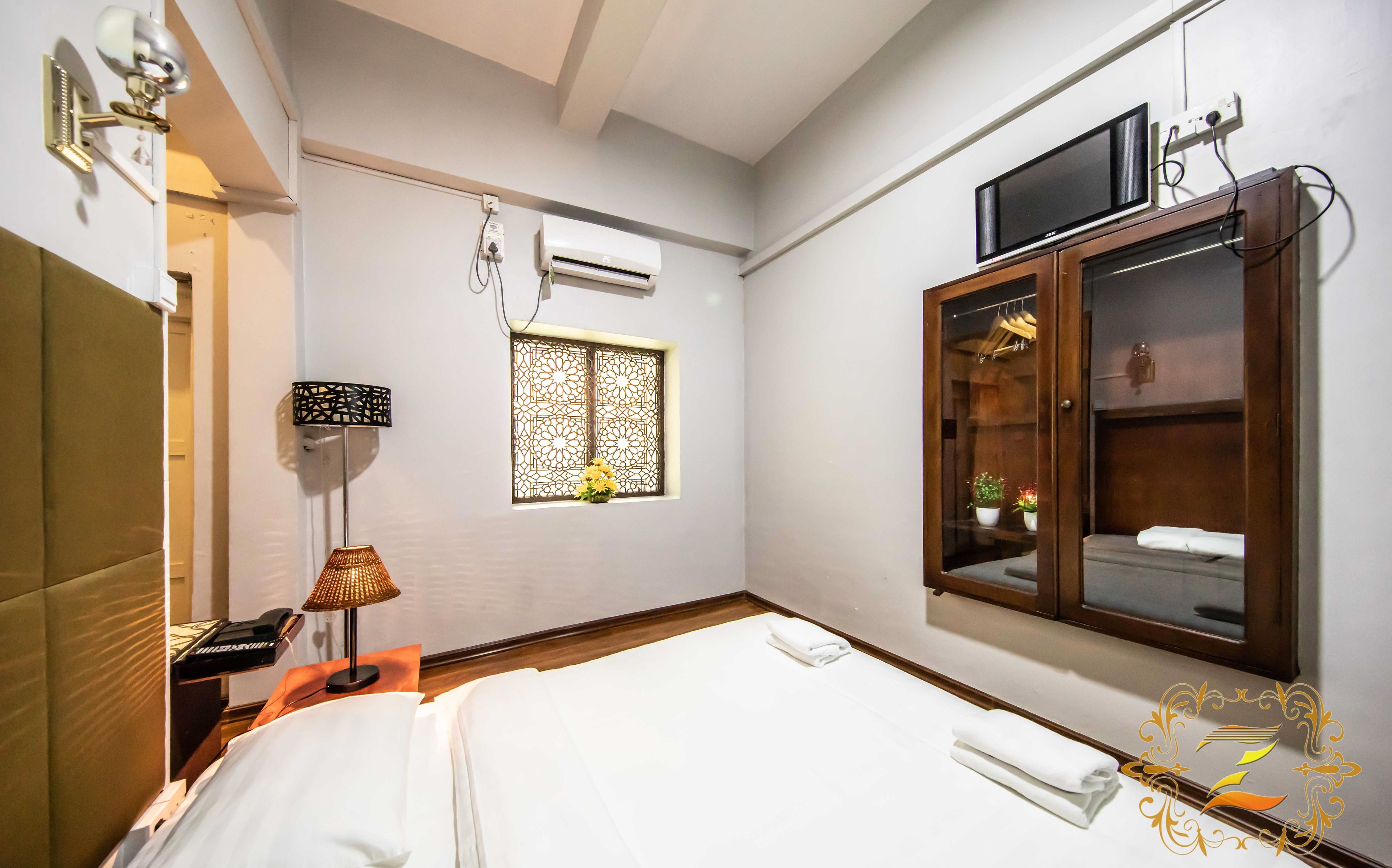 Una habitación de hotel con una cama, un escritorio con lámpara, un equipo de aire acondicionado, un televisor y un armario.