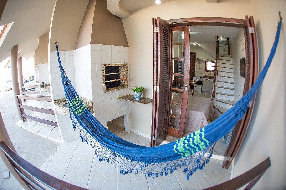 Una hamaca en una habitación con suelo de baldosas, una puerta de madera y una pequeña planta en un estante.