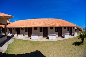 A building with a red-tiled roof, a covered patio area with seating, and a well-maintained lawn. - Pousada Brisa do Mar (Imbituba)