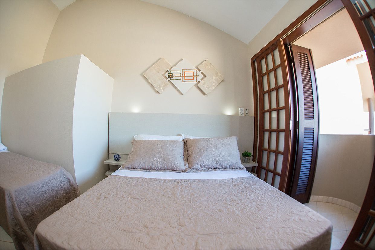 Quarto com cama, duas mesinhas de cabeceira, um criado-mudo e uma obra de arte na parede.