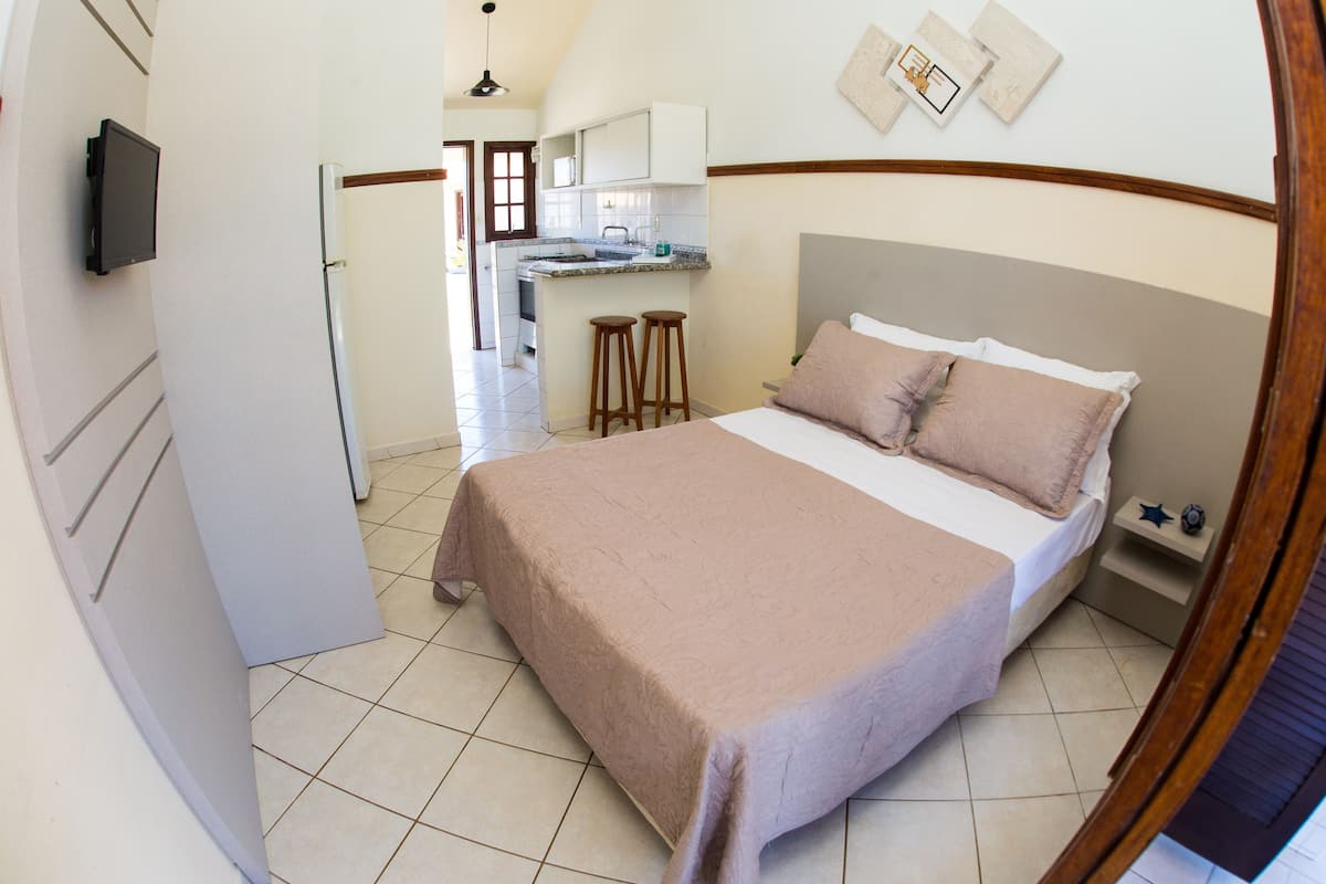 Un dormitorio con cama, una kitchenette pequeña y un televisor montado en la pared.
