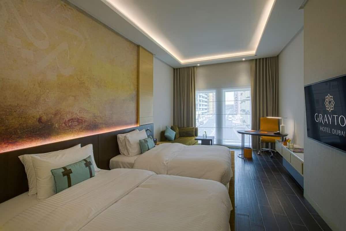 A hotel room with two beds, a desk, a chair, and a large window with curtains.