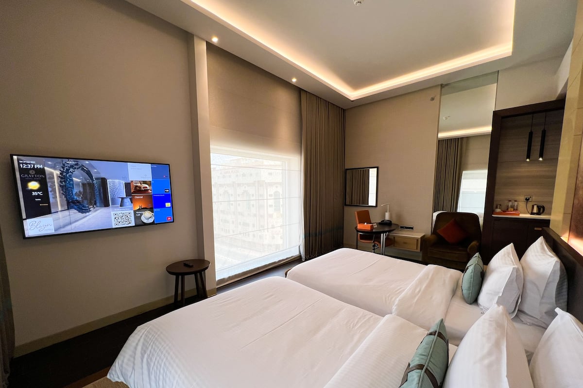 A hotel room with a large bed, a desk, a chair, a TV mounted on the wall, and a window with curtains.