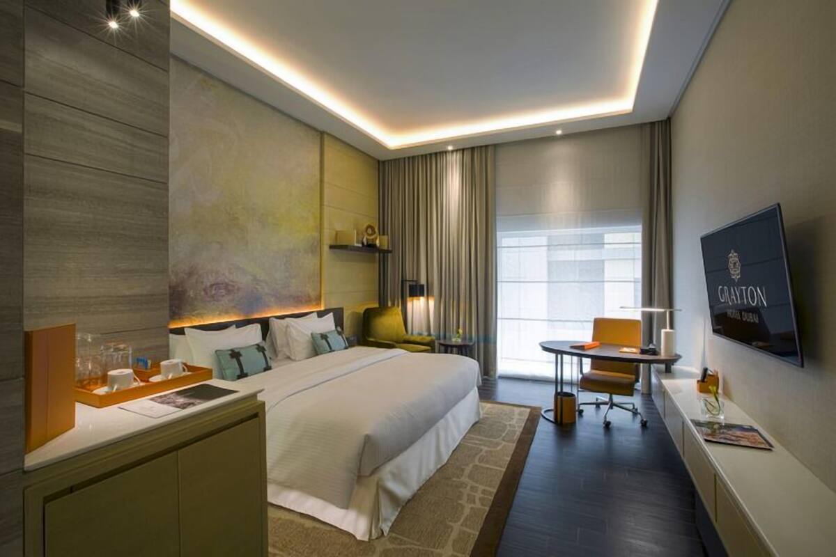 A modern hotel room with a large bed, a desk, a chair, a TV, and a window with curtains.