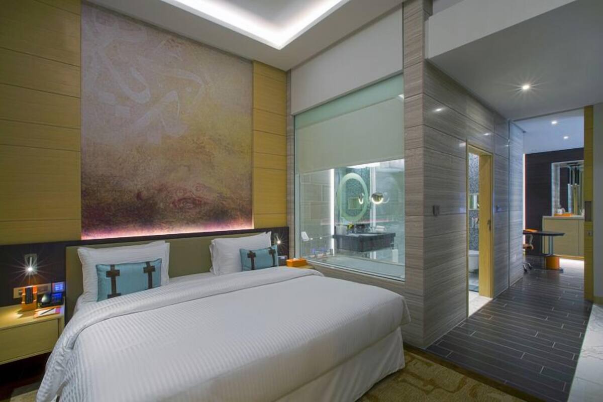 A modern hotel room with a large bed, a glass shower enclosure, and a view of the cityscape.