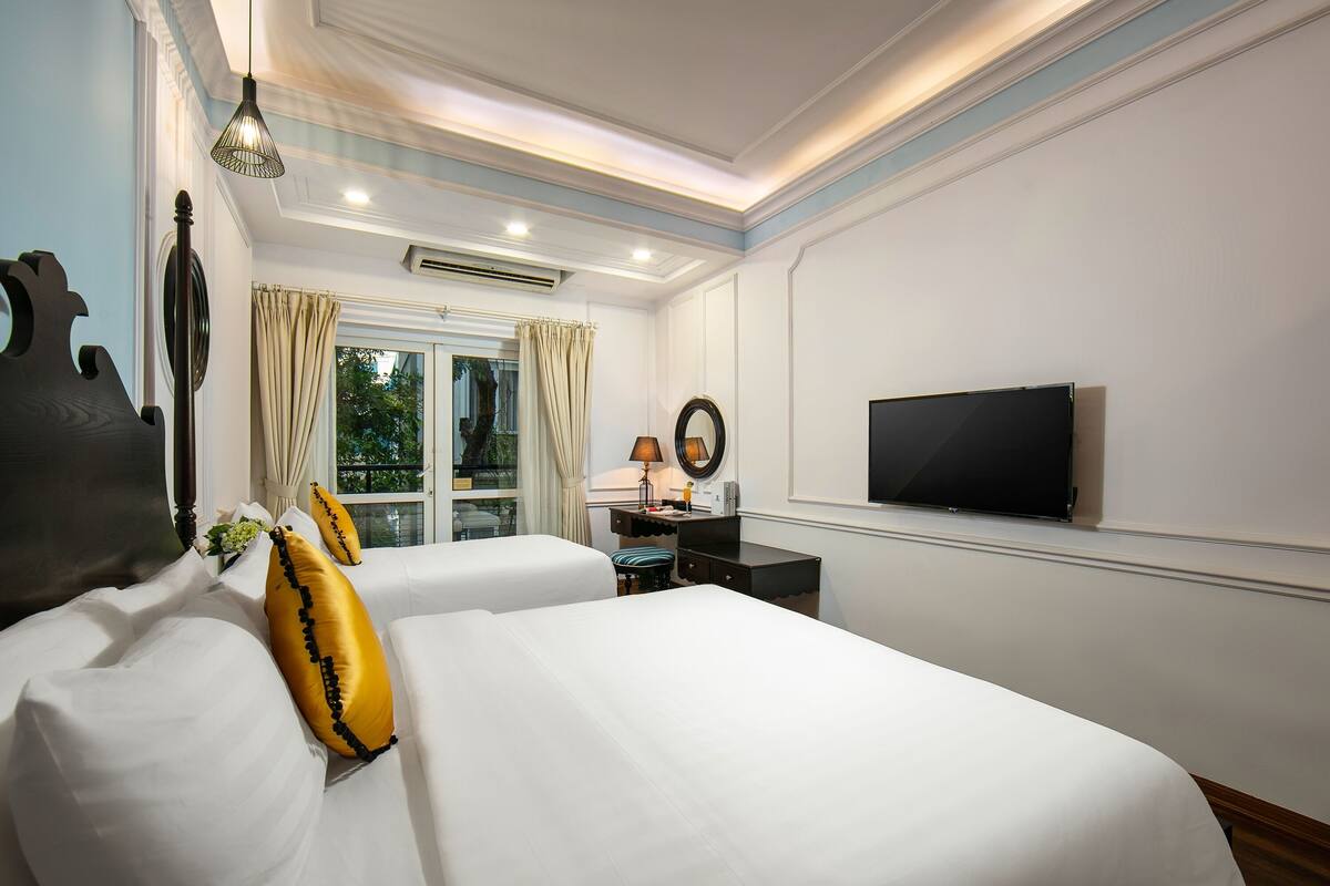 Une chambre d’hôtel avec deux lits, une télévision, un bureau avec une lampe et une fenêtre avec des rideaux.
