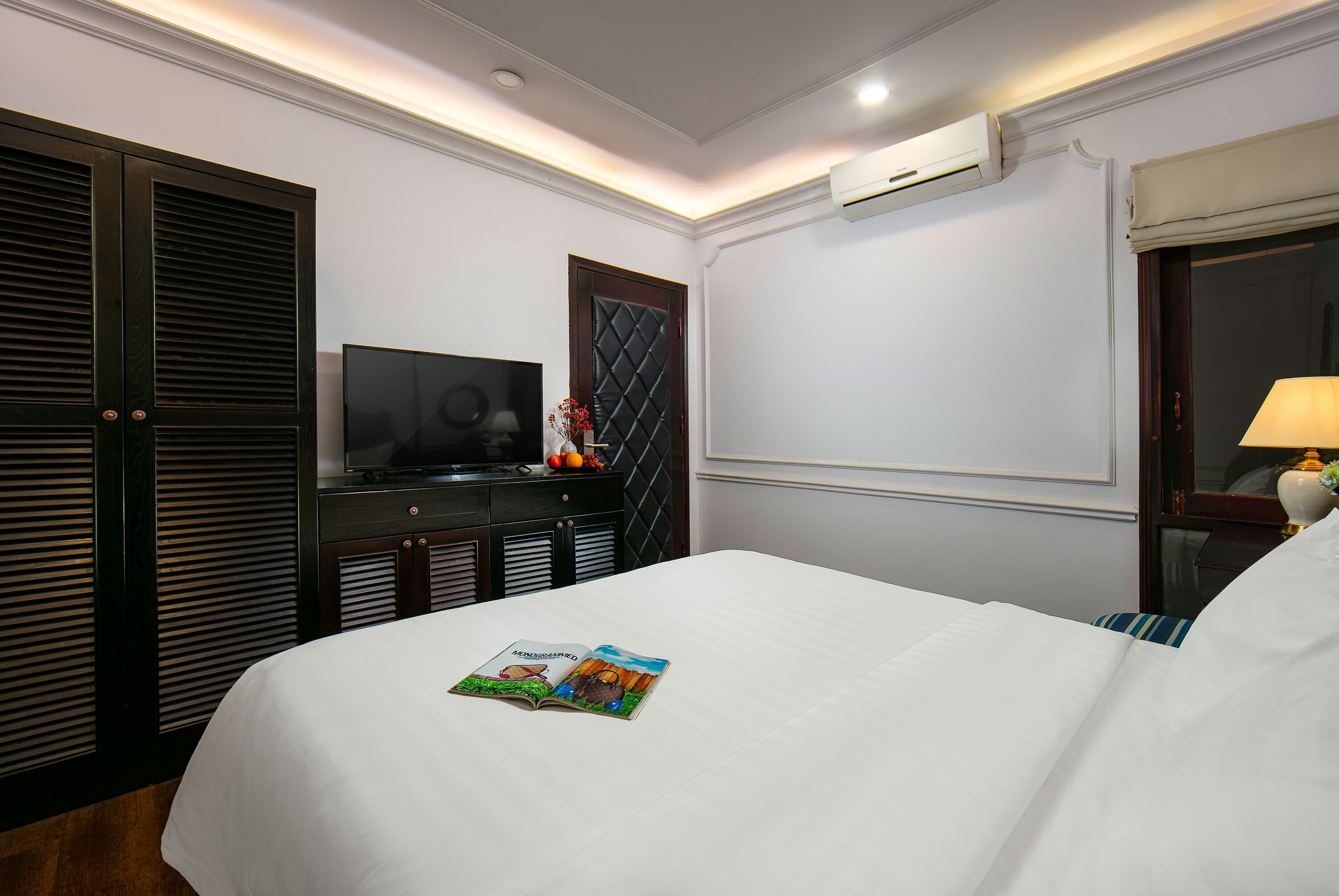 Una habitación de hotel con una cama, televisor, cómoda y equipo de aire acondicionado.