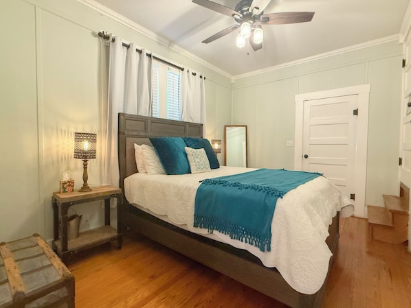 A bedroom with a bed, a nightstand, a lamp, a ceiling fan, and a door.