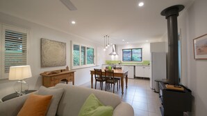 Een moderne woonkamer met een bank, een eethoek met een tafel en stoelen, een keuken met een fornuis en een koelkast, en een schoorsteen.
