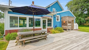 Une maison bleue avec une terrasse en bois, une table de pique-nique et un grand parasol.