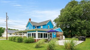 Une maison à deux étages, avec une façade bleue, un porche couvert et une petite terrasse.